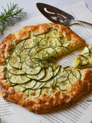 Angled view of zucchini ricotta galette with a slice cut out on a white background