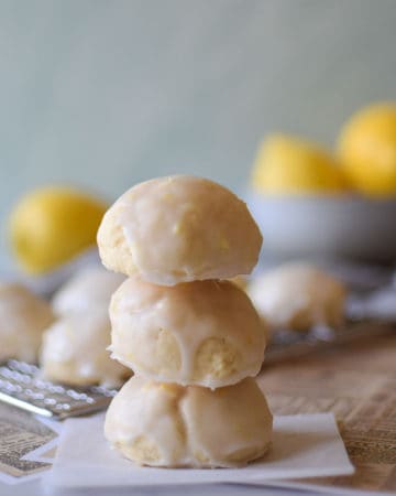 Italian lemon drop cookies stacked with 3 cookes and lemons in the background