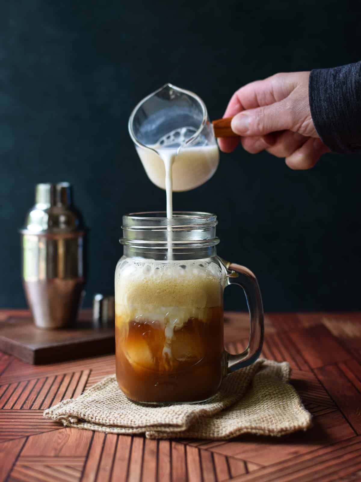 Milk being poured into a clear mug with chai tea.