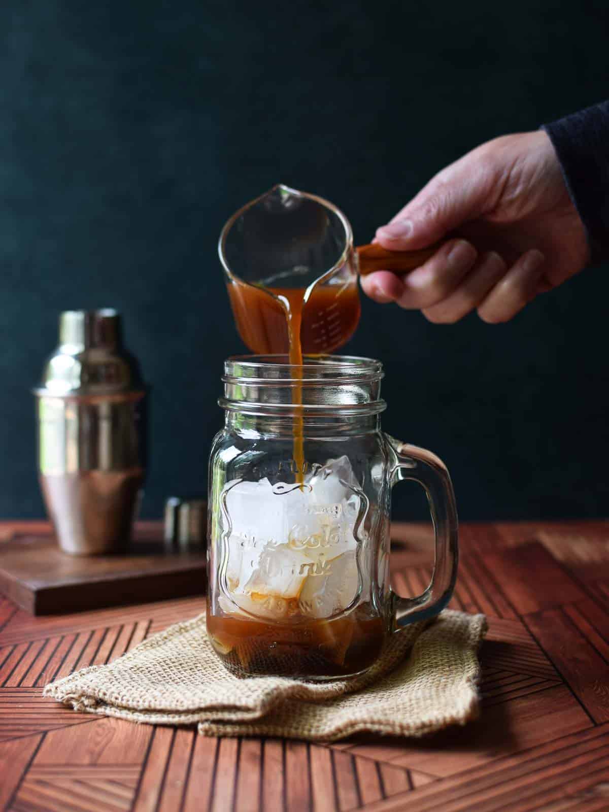 Chai concentrate being poured into a mug with ice.