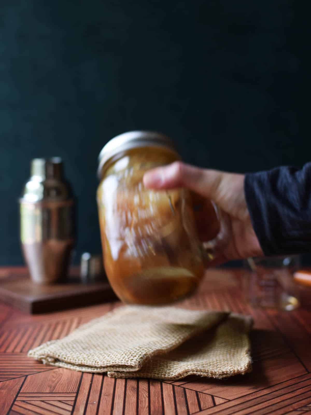 A hand shaking a mason jar mug with ice, sugar, and chai tea.