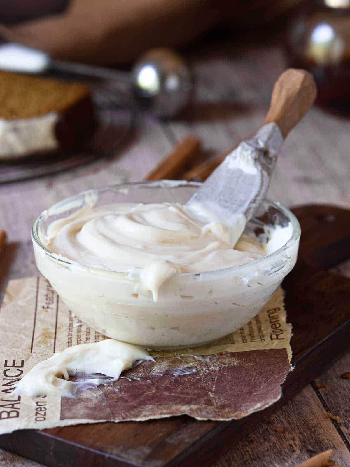Cream cheese frosting in a clear bowl on a wood surface.