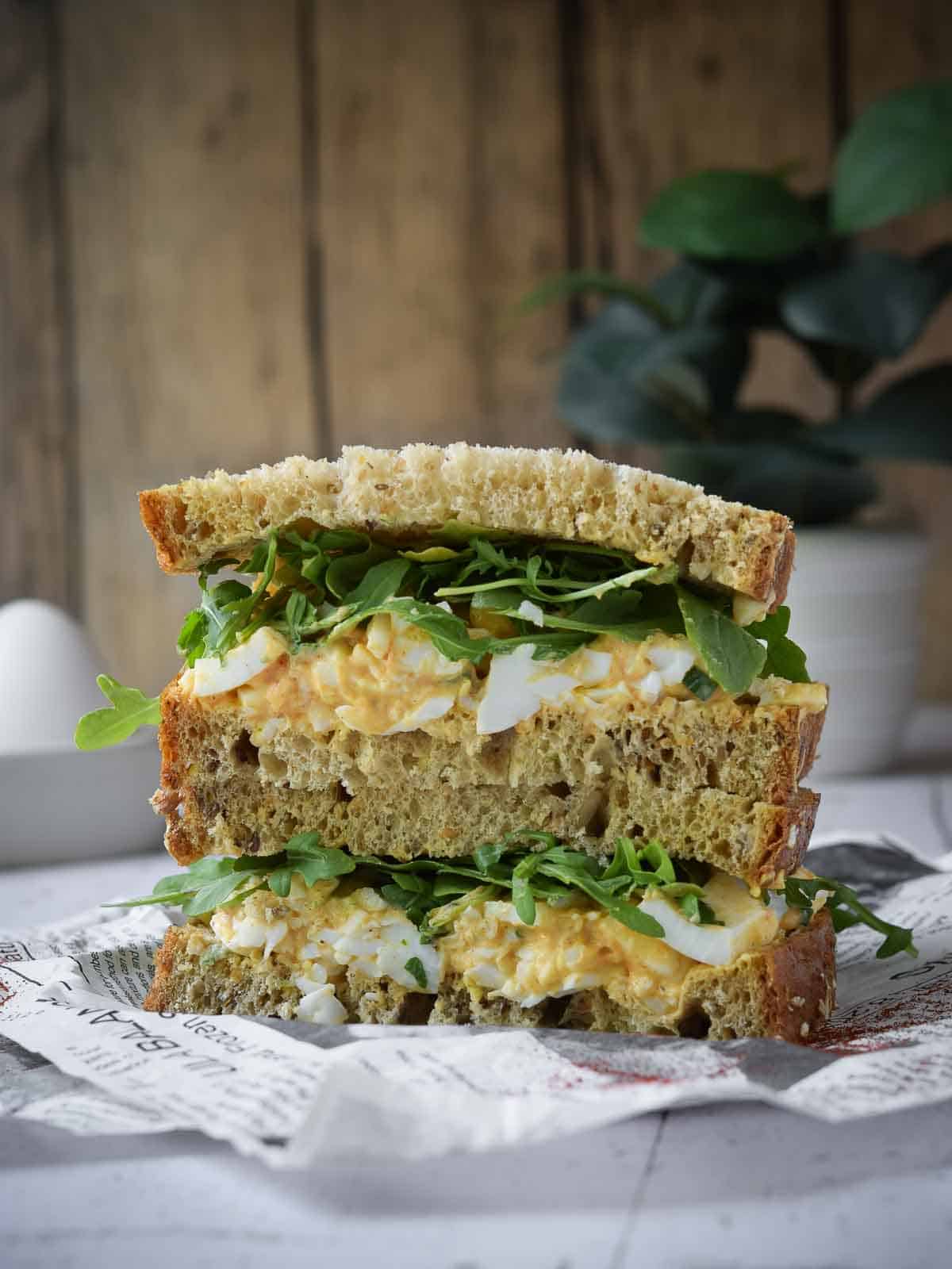 Egg salad sandwich stacked on deli paper with a wood background.