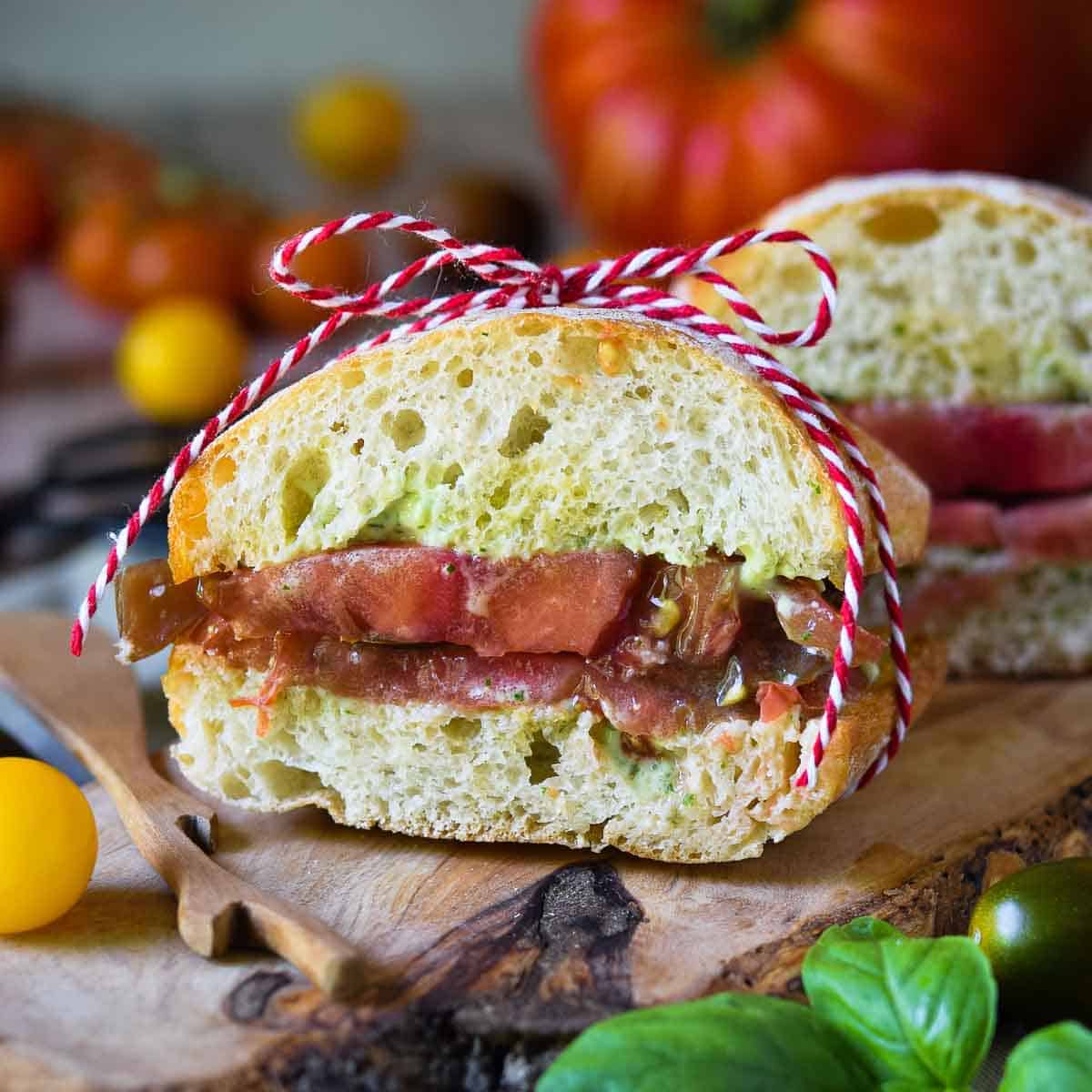 Tomato sandwich on a wood board tied up with a string.