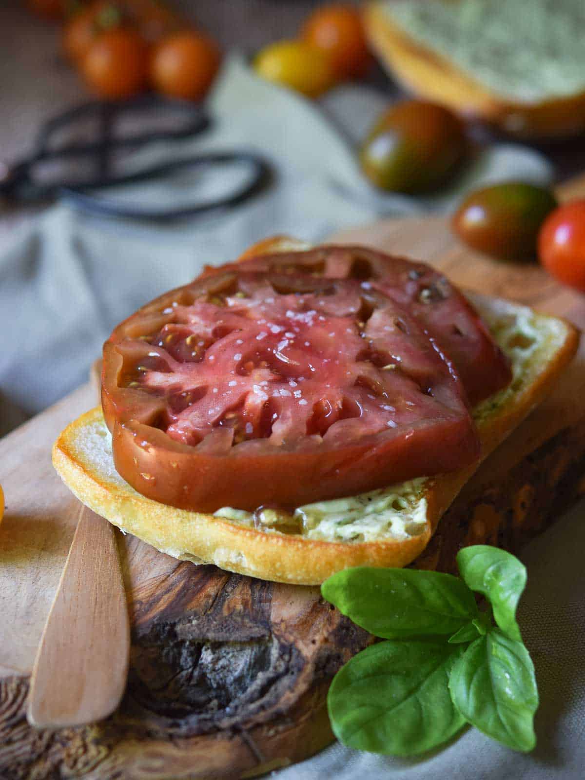 Sliced red tomatoes on bread with pesto mayo on a wood board.