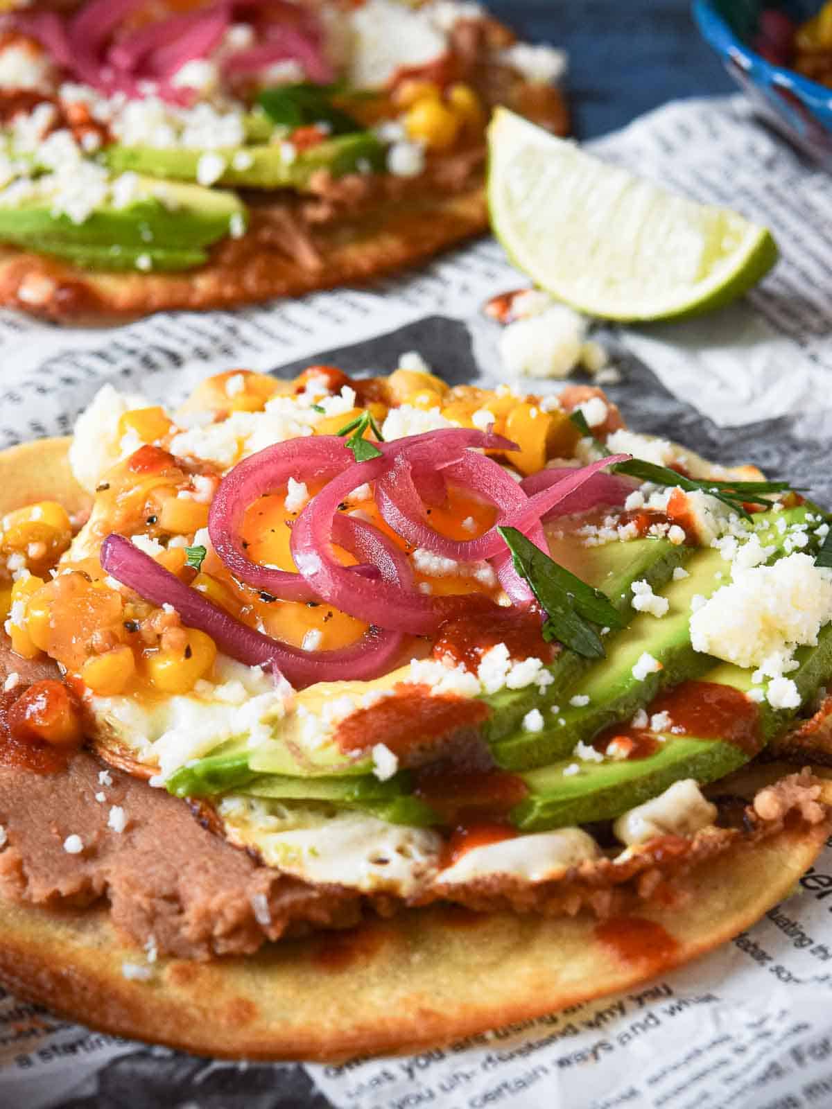 Huevos rancheros tostadas on newspaper with a lime in the background.