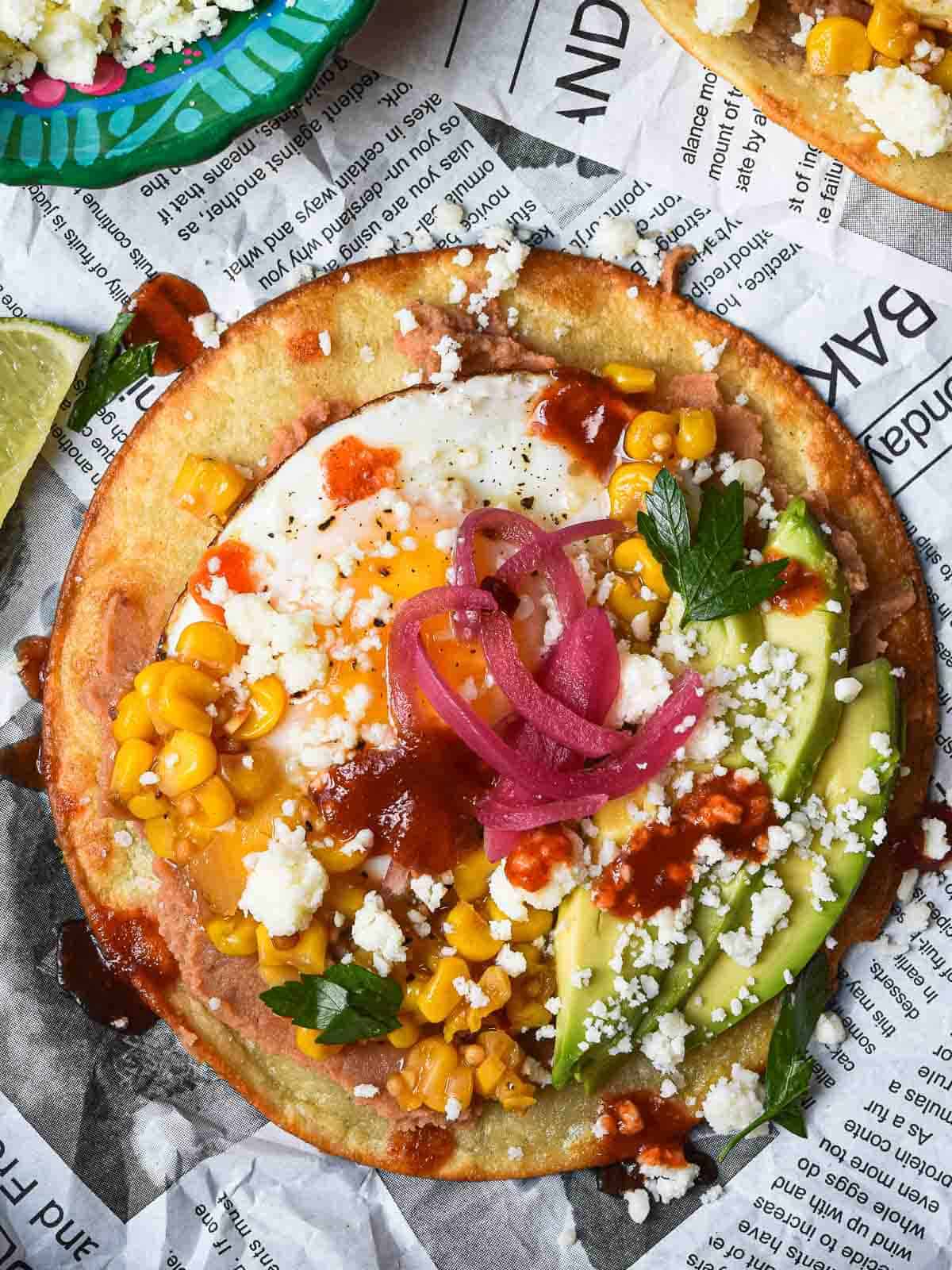 Overhead view of a Mexican tostada with toppings on newspaper.