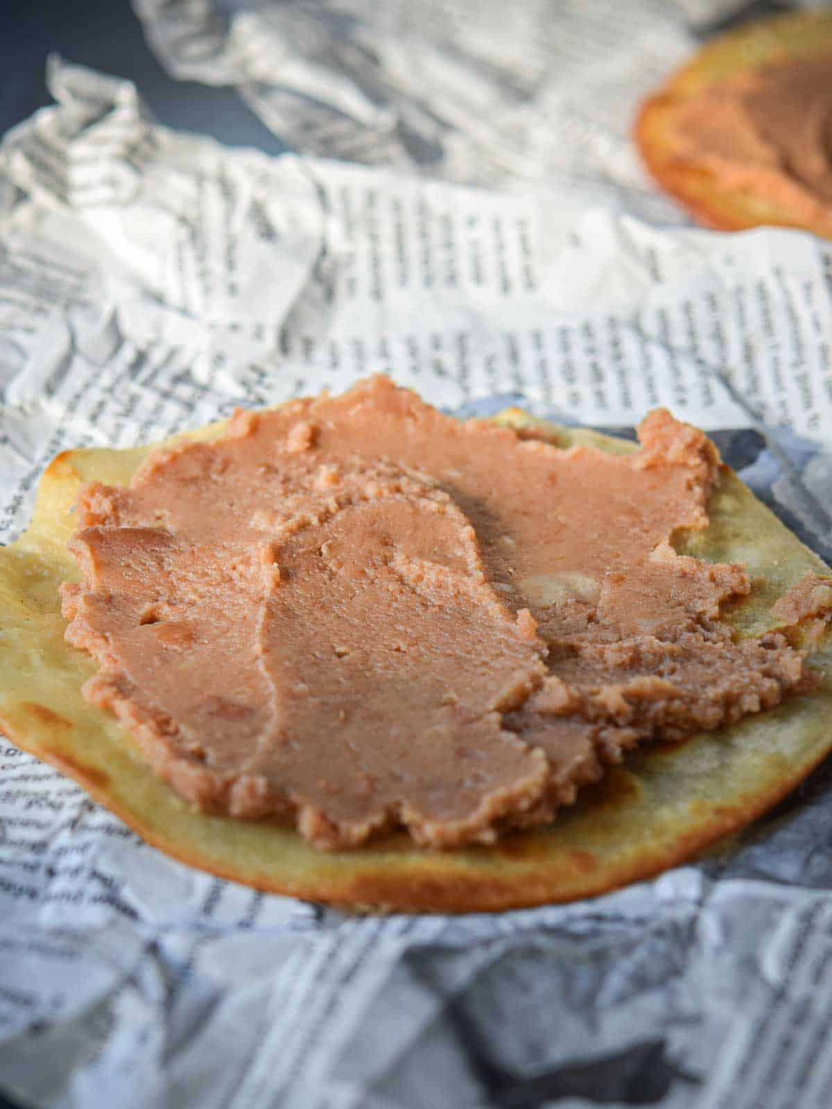 Fried tortilla with refried beans spread on top of it.