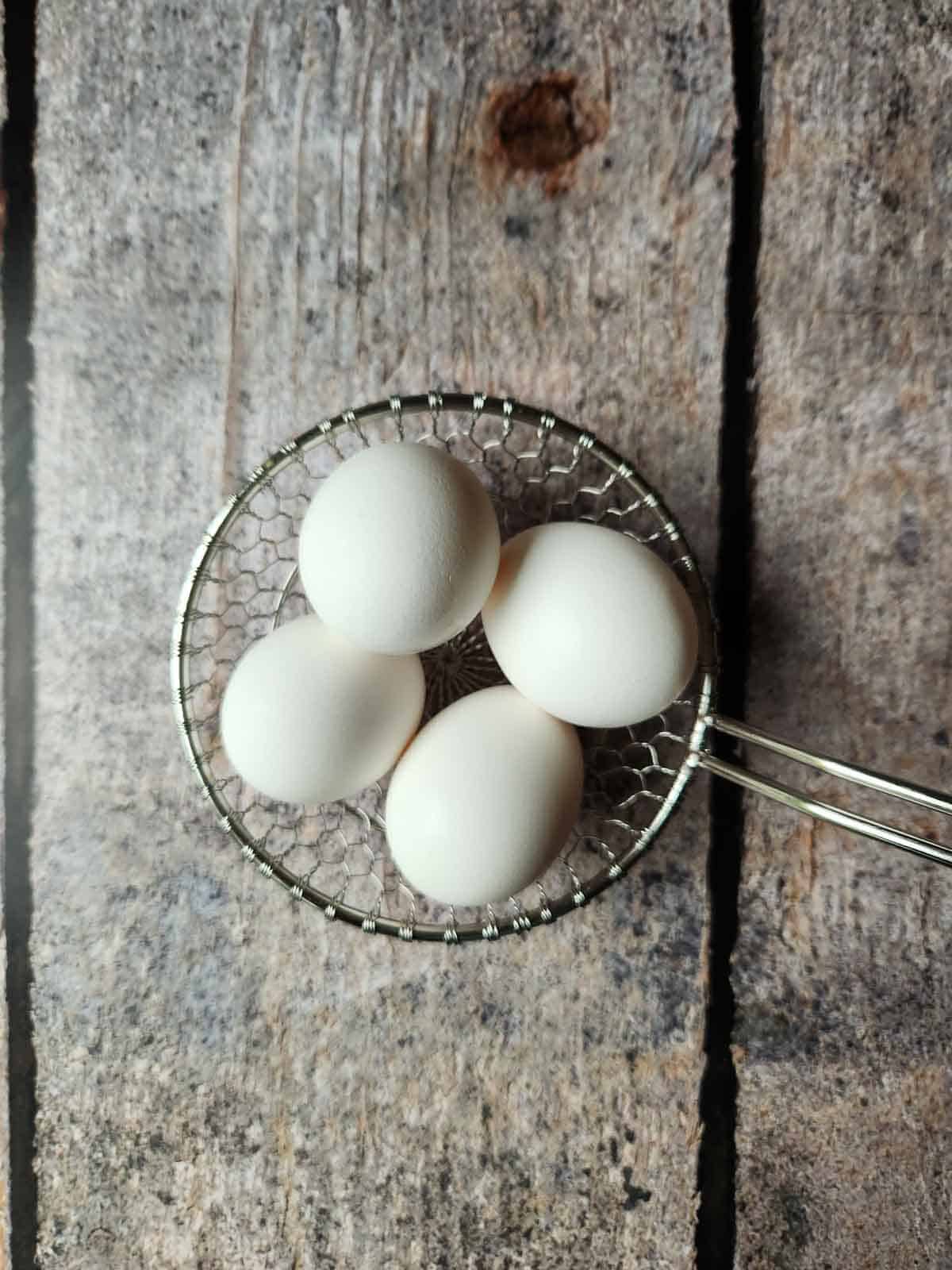 Four eggs in a wire strainer.