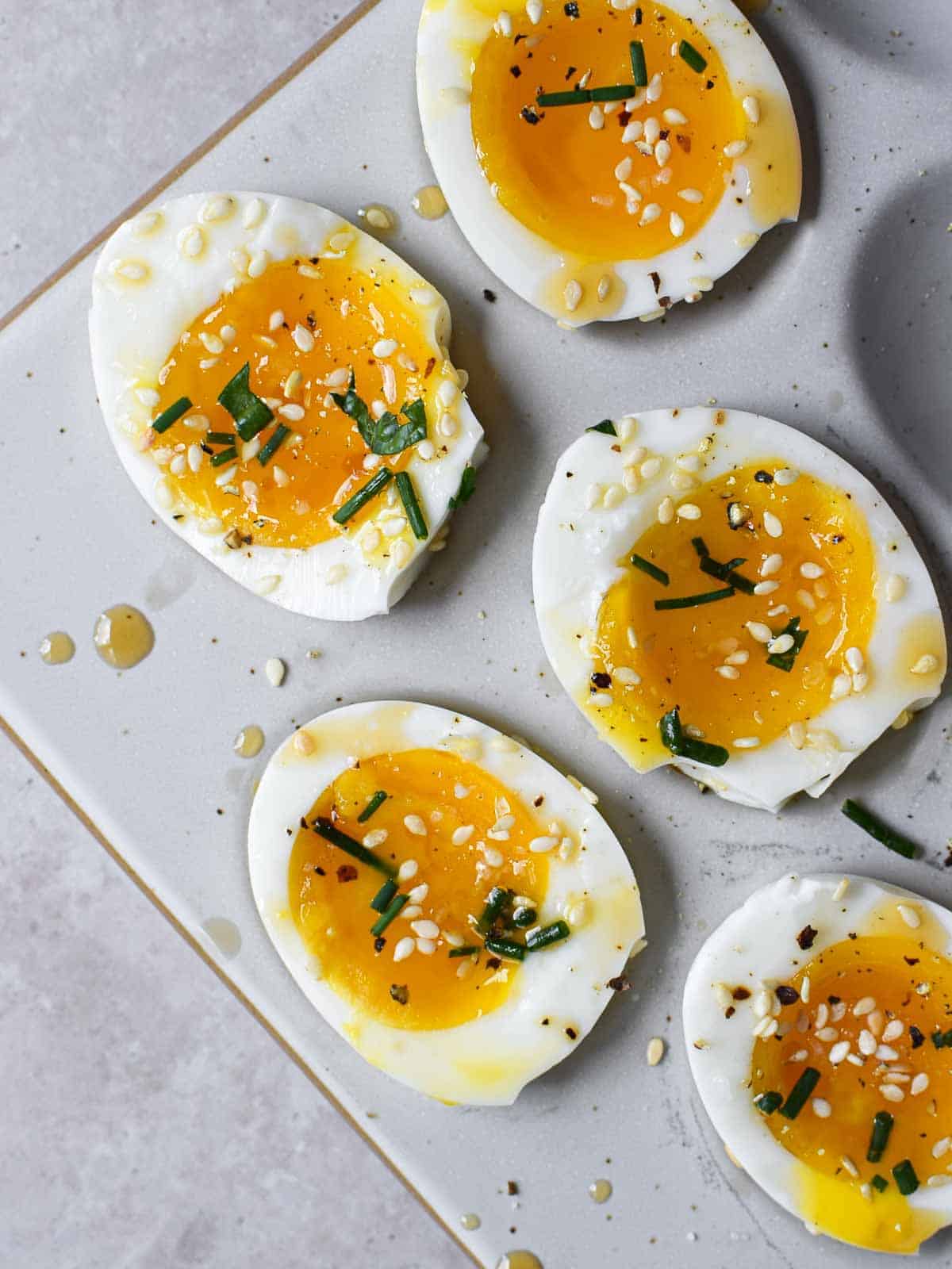 Overhead view of soft-boiled eggs with sesame oil and toasted sesame seeds cut open.