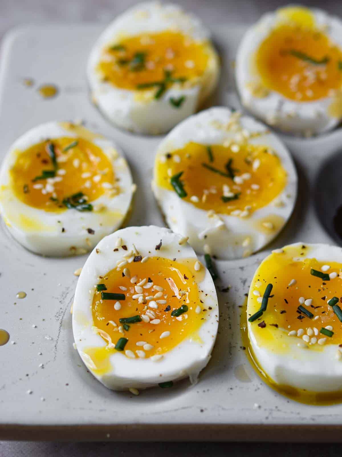 Soft-boiled eggs with sesame oil and toasted sesame seeds cut open on a platter.