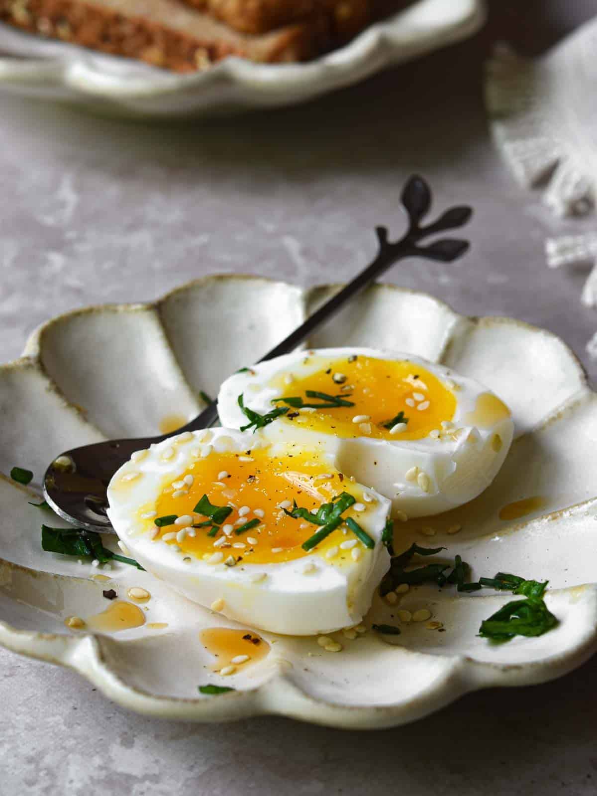 Soft-boiled eggs with sesame oil and toasted sesame seeds cut open on a beige dish.