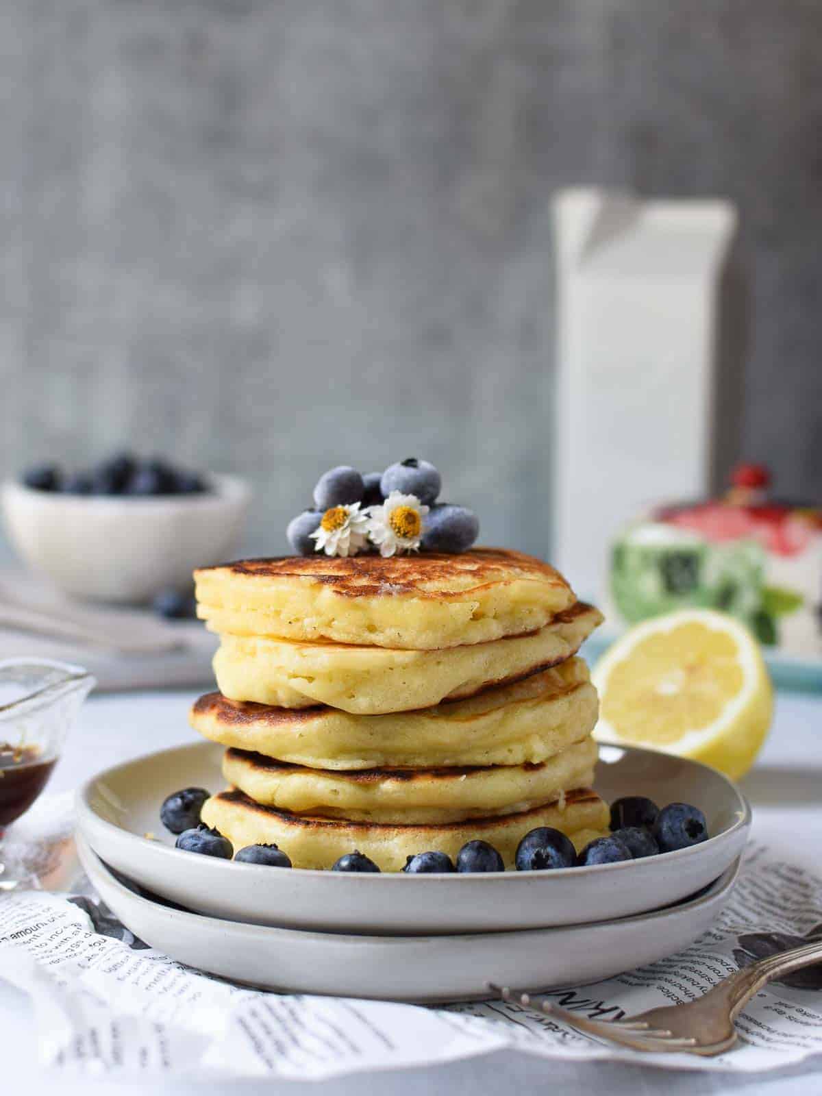 Lemon pancakes stacked on plates with blueberries on top.