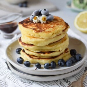 Lemon mascarpone pancakes stacked on plates with blueberries on top.