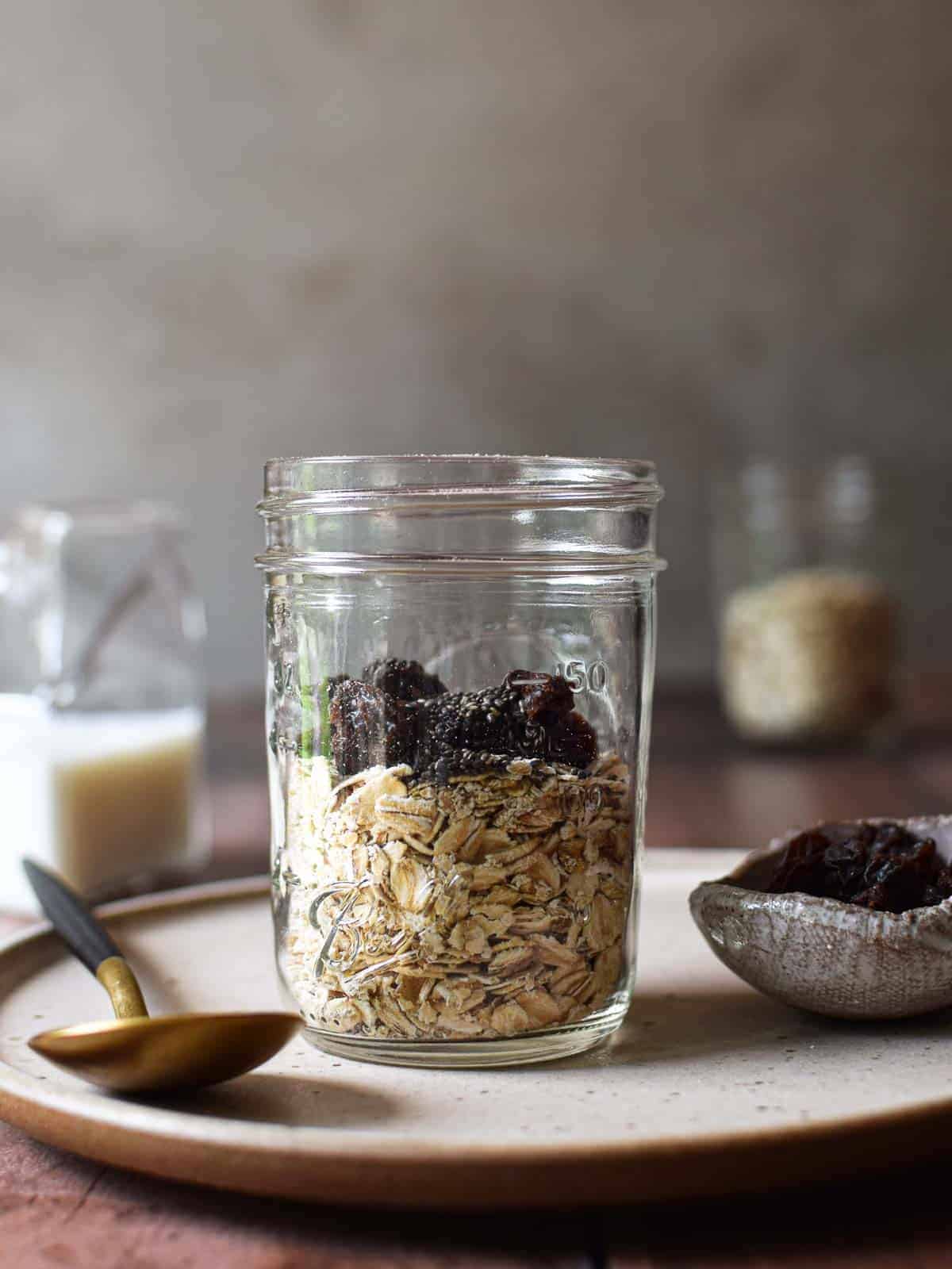 Oats and raisins in a clear jar on a beige plate.