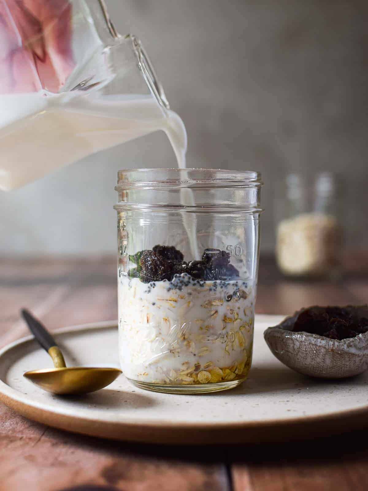 Milk is poured into a Mason jar to prepare overnight oats.