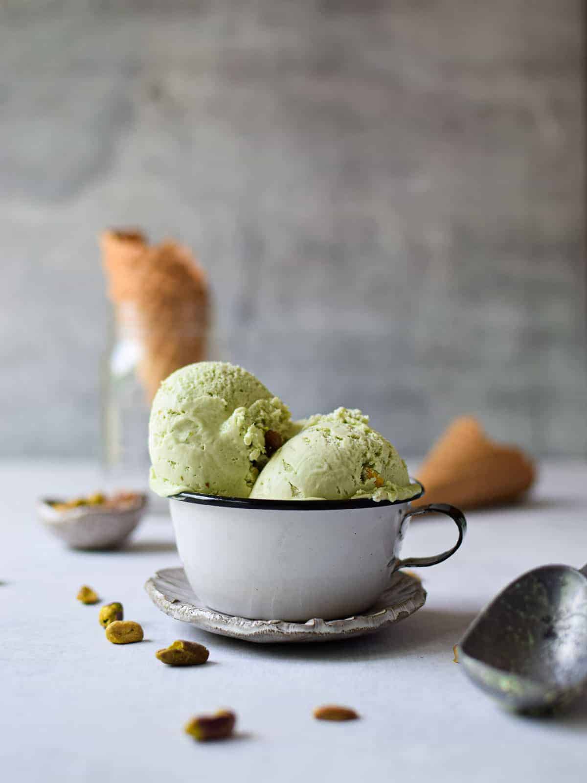 Eye level of 2 scoops of pistachio ice cream in a white cup.