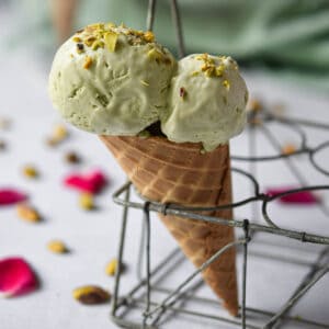 Pistachio ice cream on a waffle cone in a metal holder.