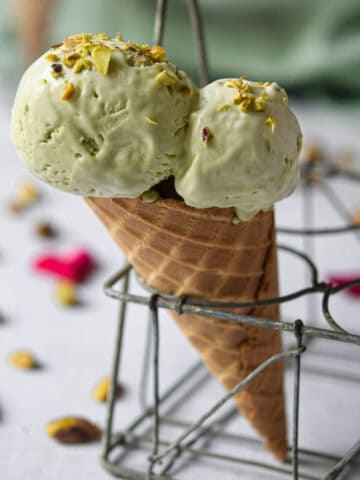 Pistachio ice cream on a waffle cone in a metal holder.