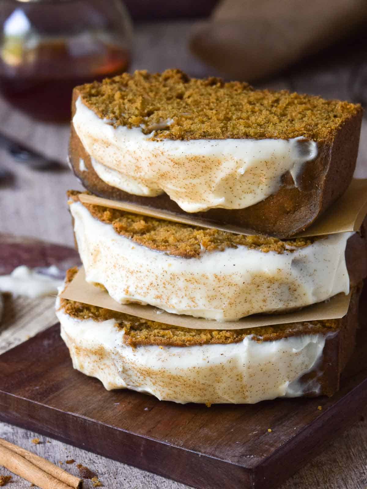 Three slices of pumpkin bread with maple cream cheese frosting stacked on top of each other.