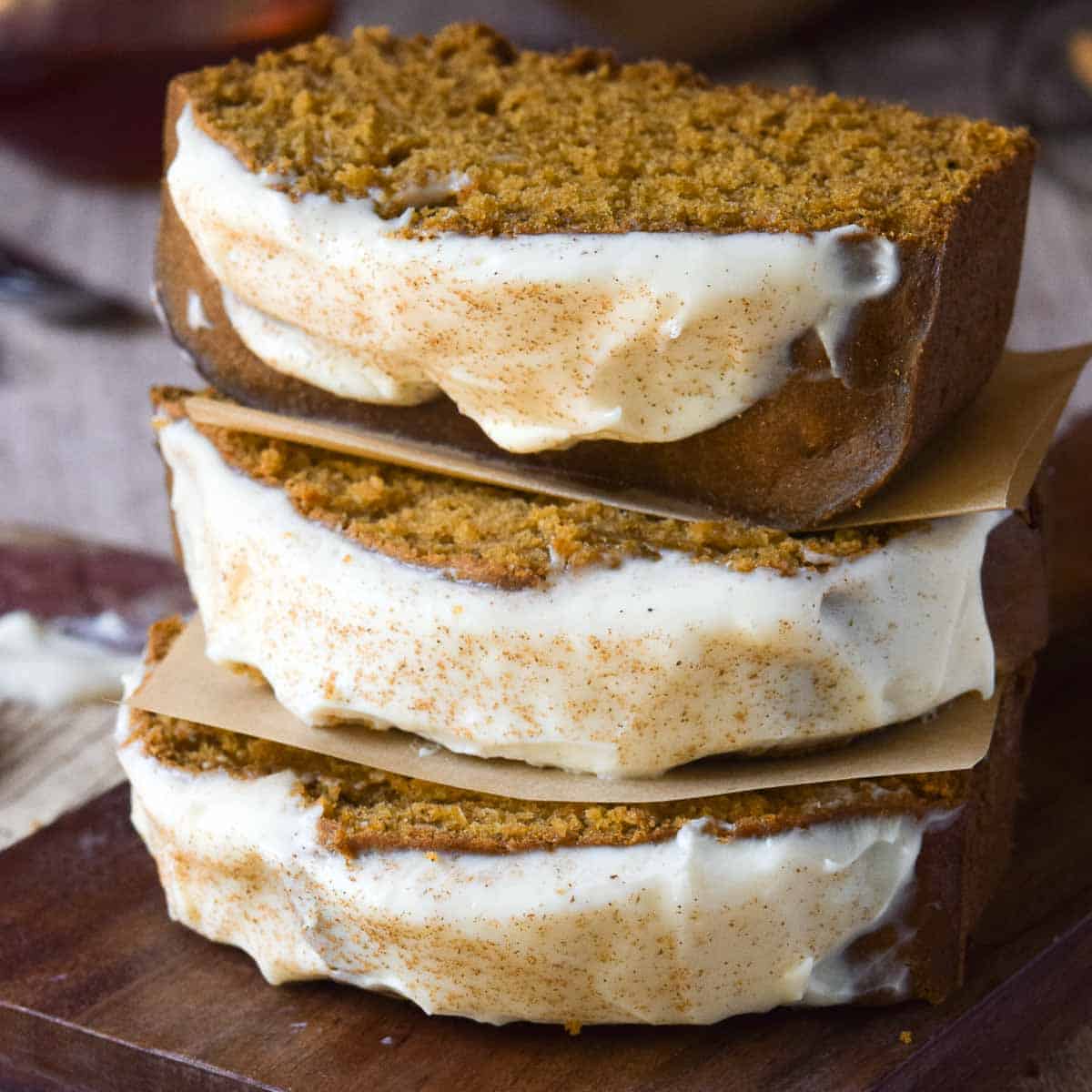 Three slices of pumpkin bread stacked on top of each other on a wood board.