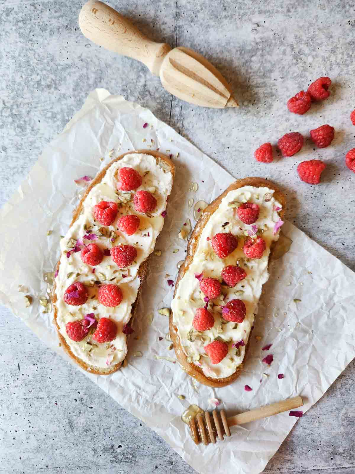 Two slices of raspberry and ricotta toast on white parchment paper.