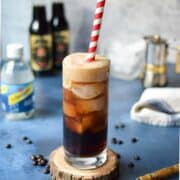 Espresso soda in a glass with a red straw on top of a blue surface.