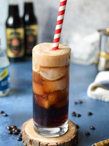Espresso soda in a glass with a red straw on top of a blue surface.