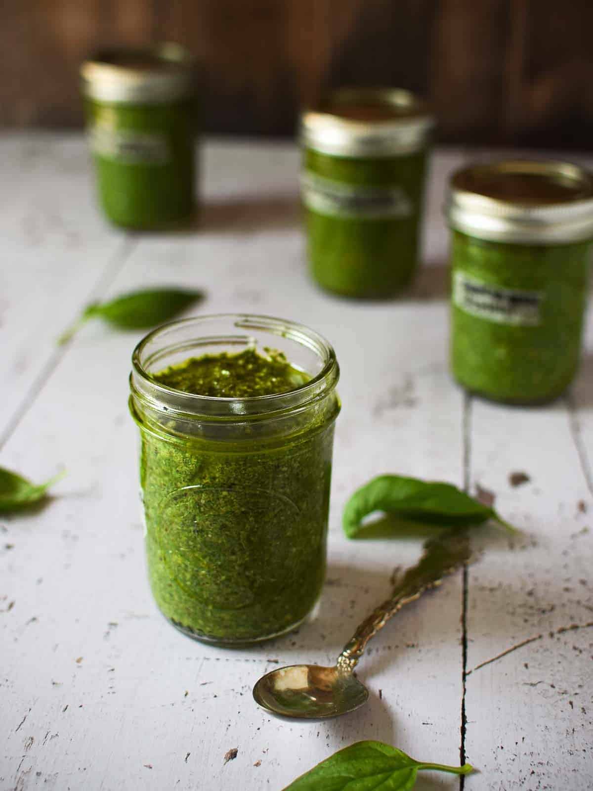 Multiple jars of pesto sauce in clear jars on a wooden surface.