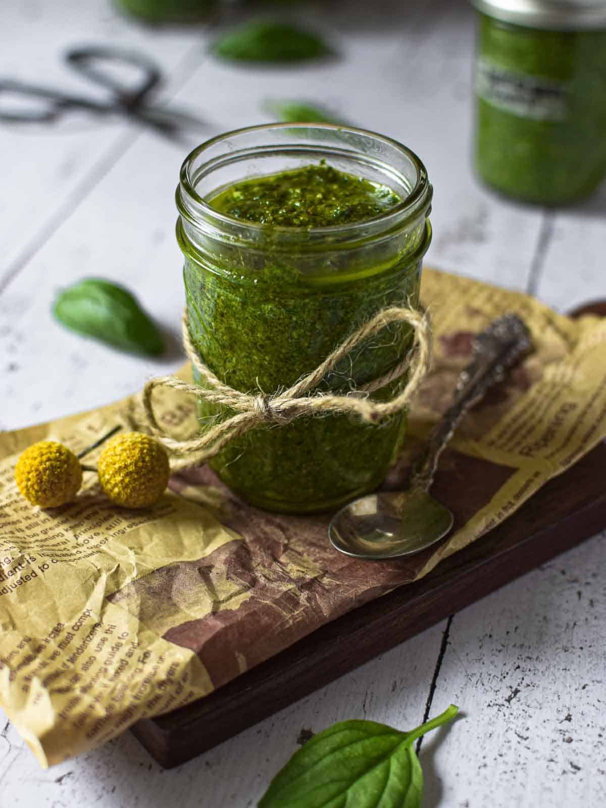 Angled view of pesto sauce in a small clear jar on a wooden surface.