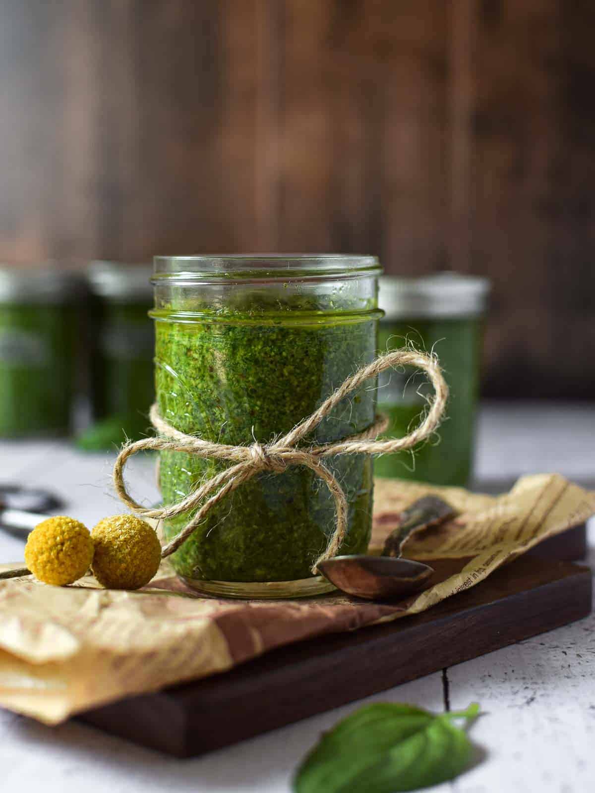 Eye-level view of pesto sauce in a clear jar on a wooden surface.