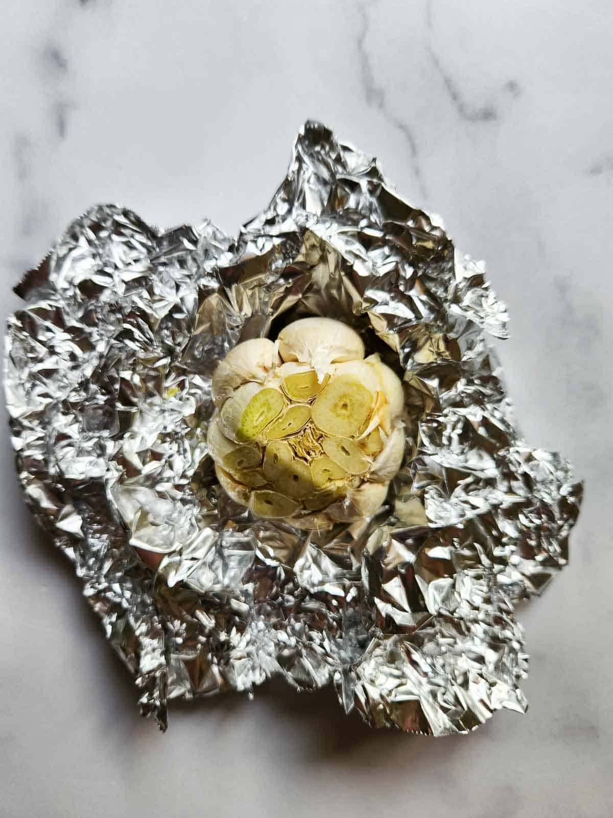 Raw garlic with top cut in aluminum foil.