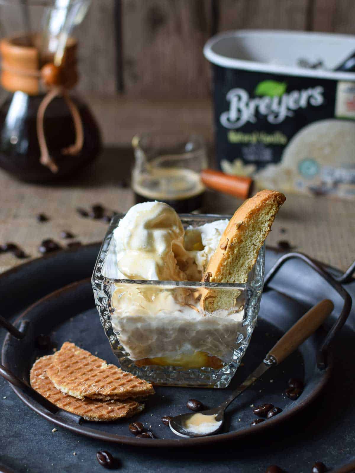 Affogato in a clear dish with a biscotti cookie in it on a grey tray.