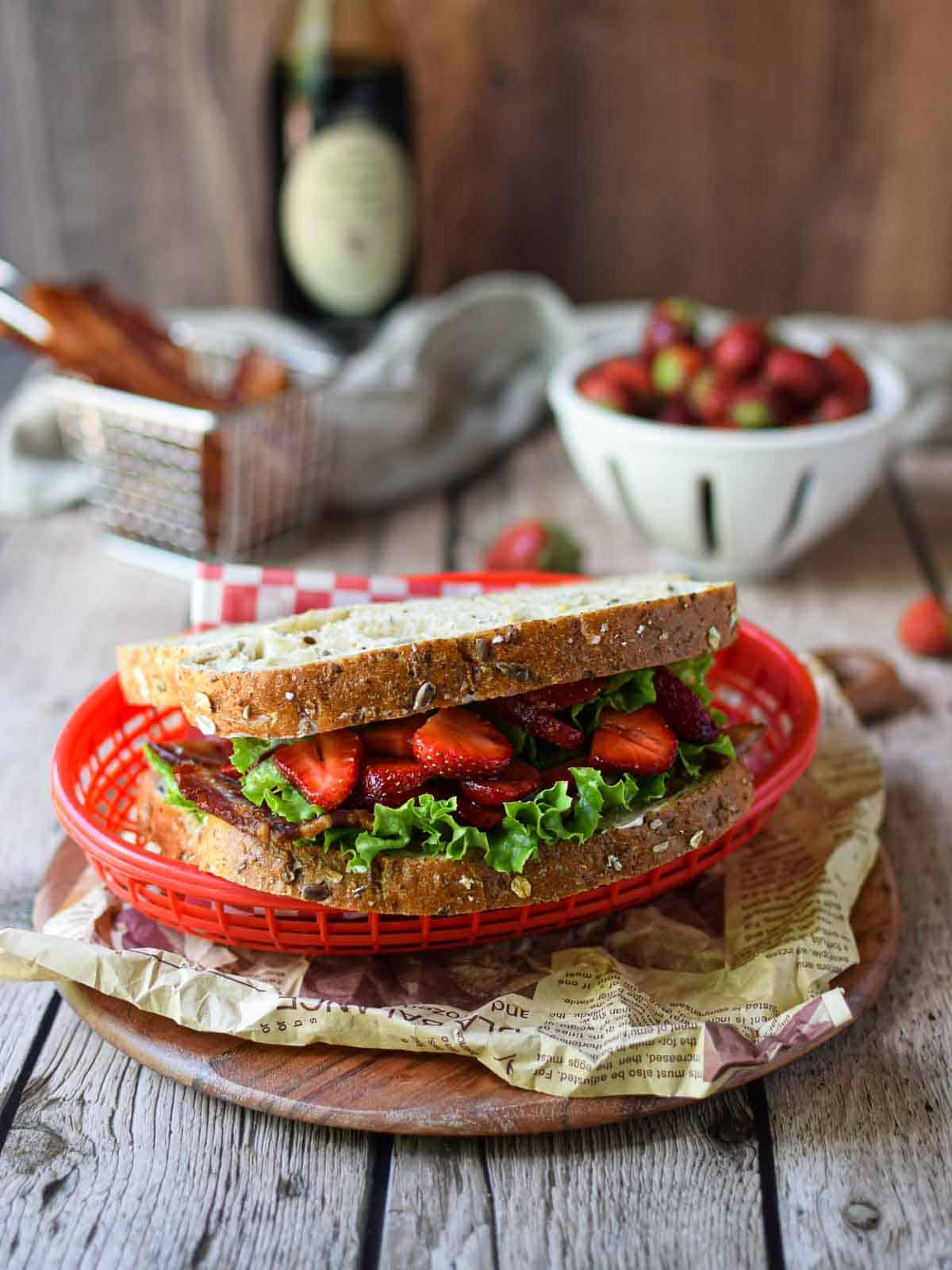 Strawberry BLT shown in a red wire basket on a wood background.