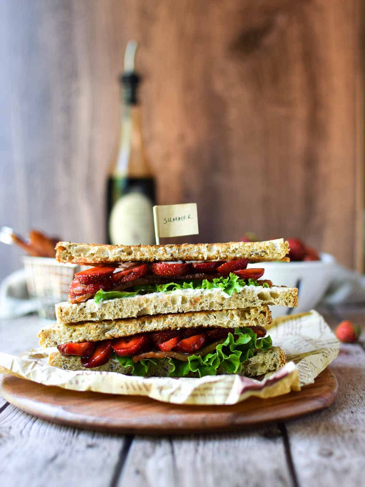 Eye-level view of strawberry balsamic BLT on a wood board stacked on top of each other.