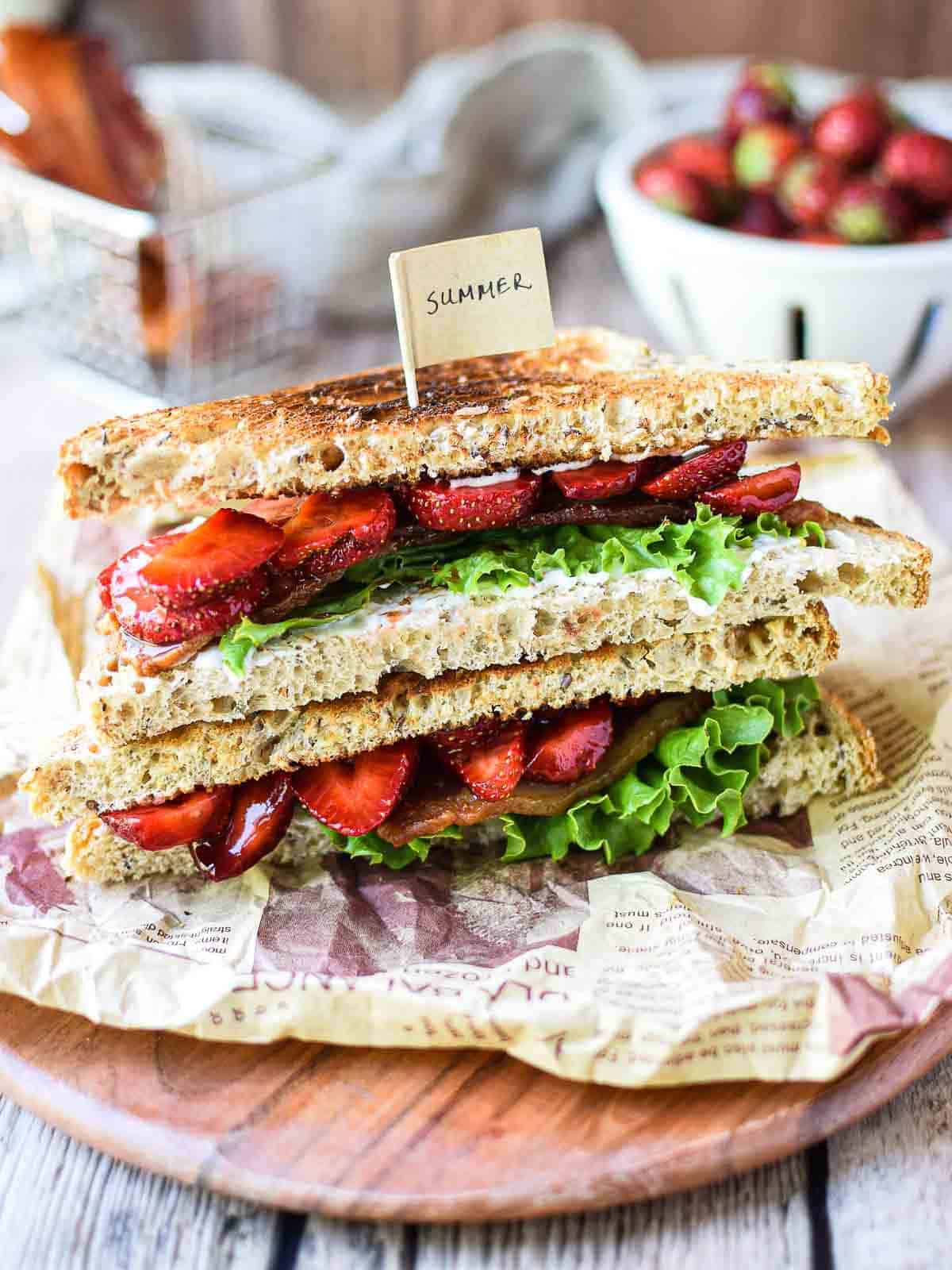 Eye-level view of strawberry balsamic BLT on a wood board stacked on top of each other.