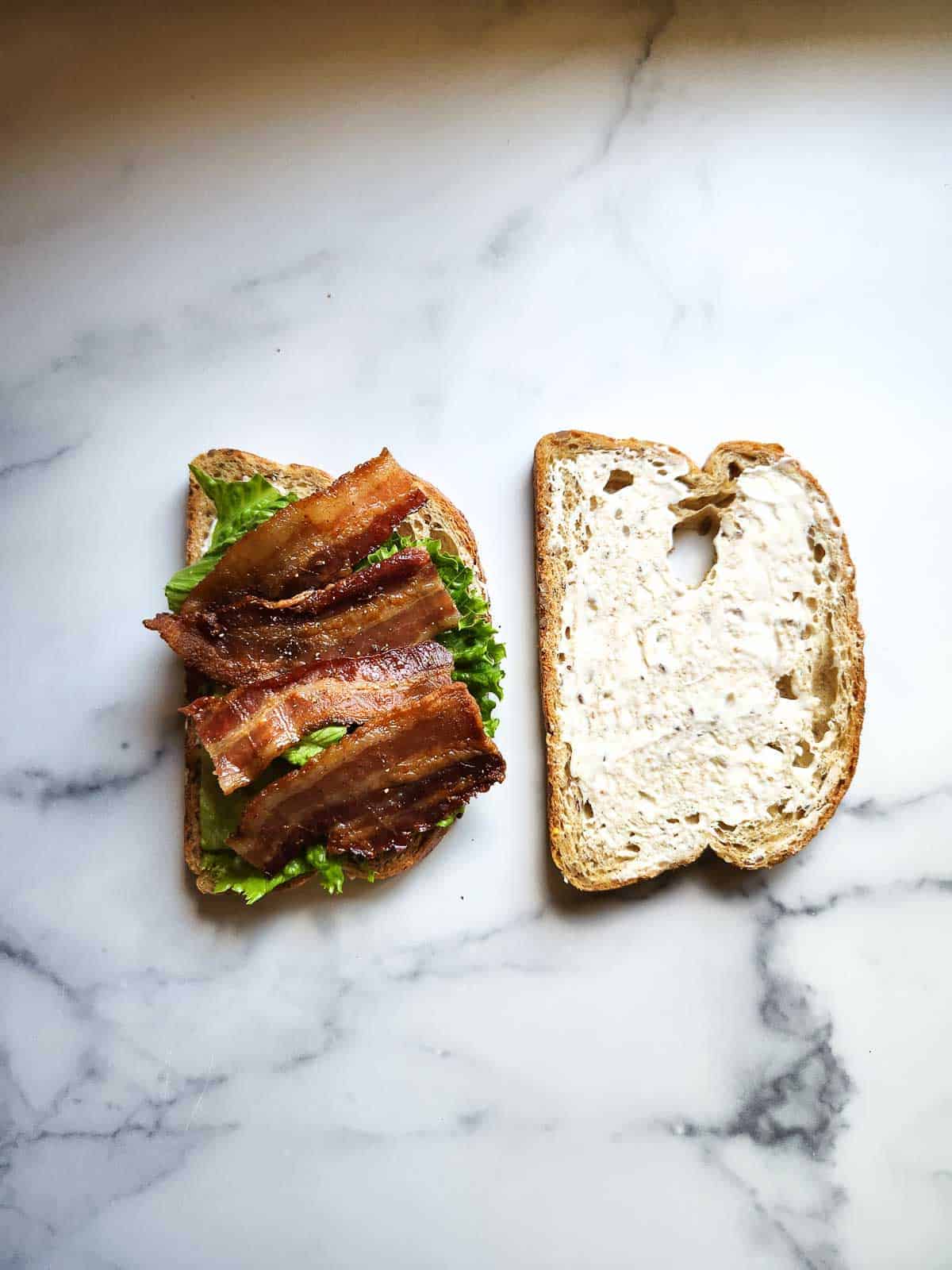 Assembling a BLT with bacon lettuce and mayo.