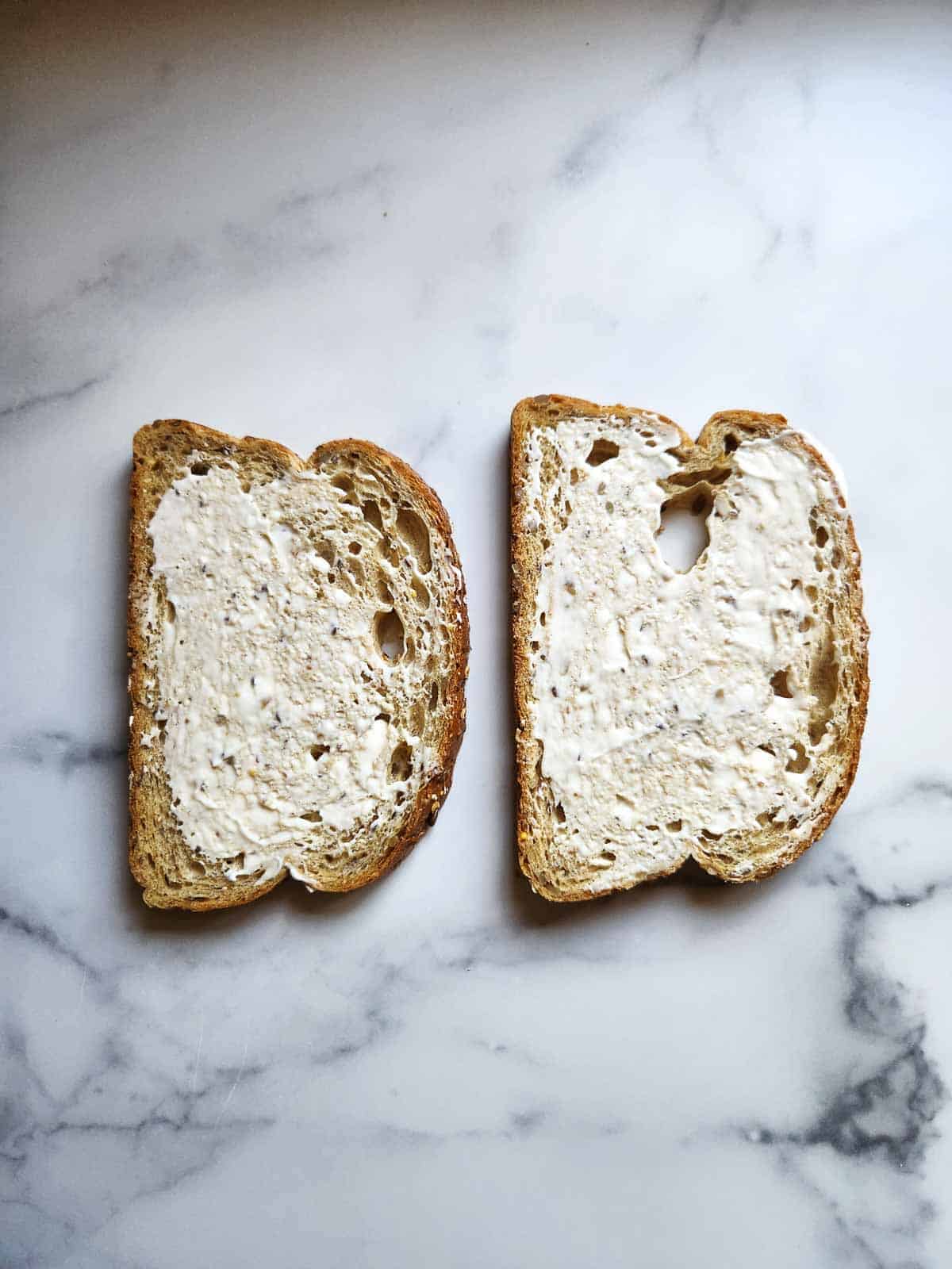 Two pieces of bread with mayo on them for a BLT.