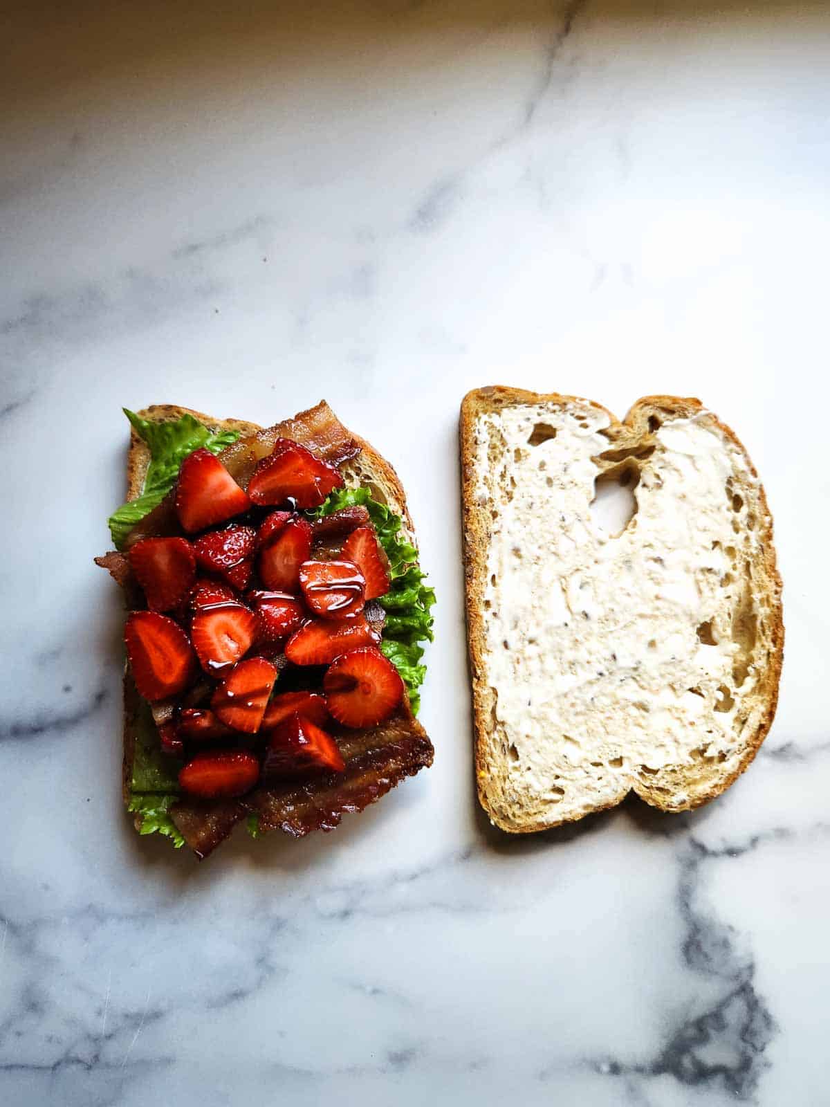 Assembling a BLT with balsamic strawberries, lettuce, bacon, and mayo.