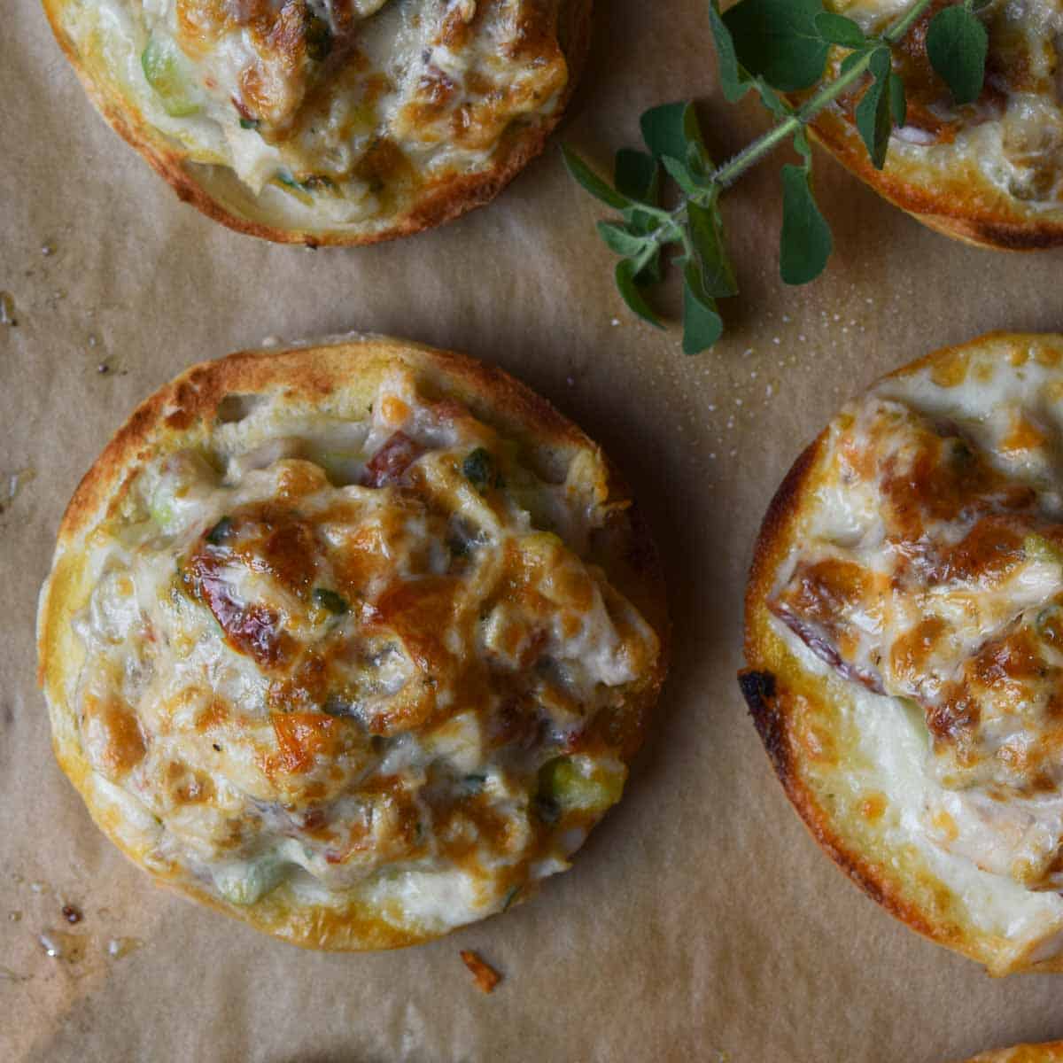 Mediterranean Sun Dried Tomato Tuna Melt 7 Overhead shot of freshly broiled Sun-Dried Tomato Tuna Melts with golden, melted cheese on parchment paper, garnished with fresh herbs, ready to serve.