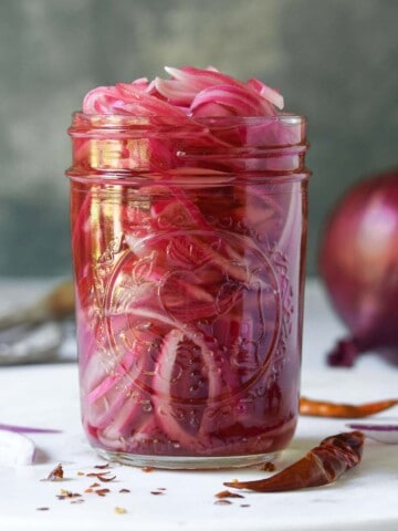 Close-up of a jar of pickled red onions on a white surface.