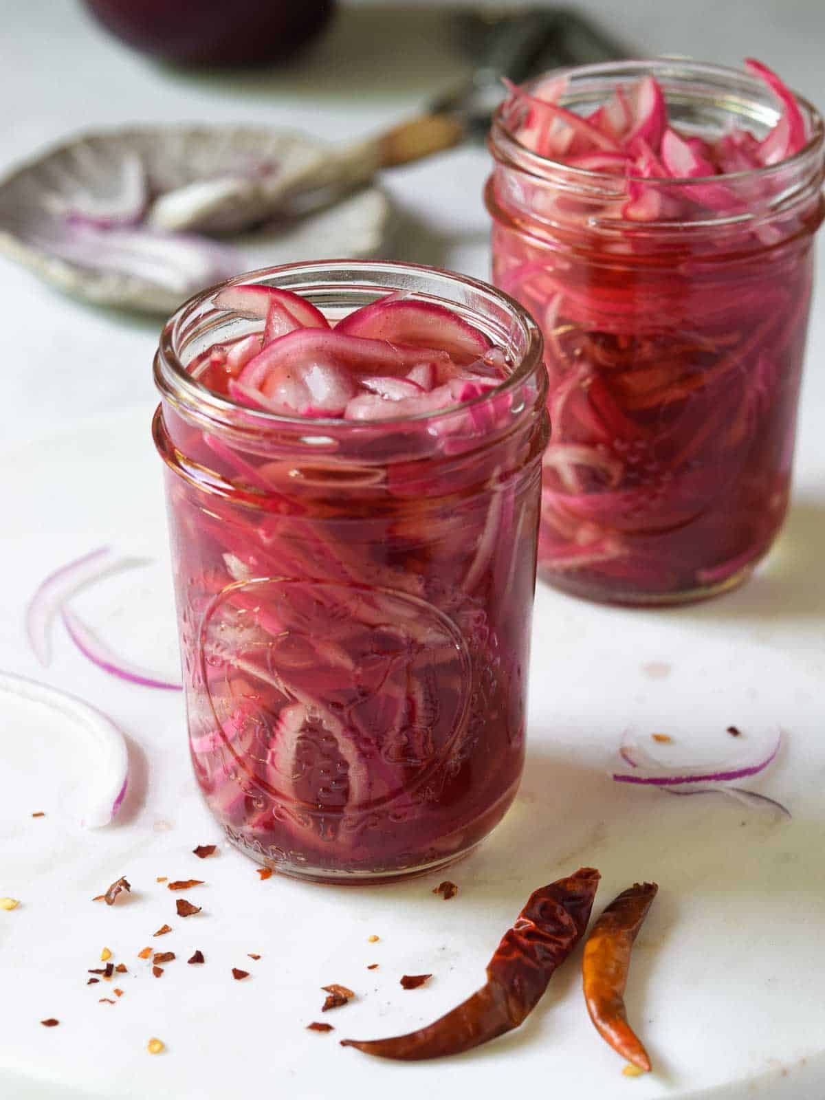 Pickled red onions in a clear Mason jar on a white marble surface.