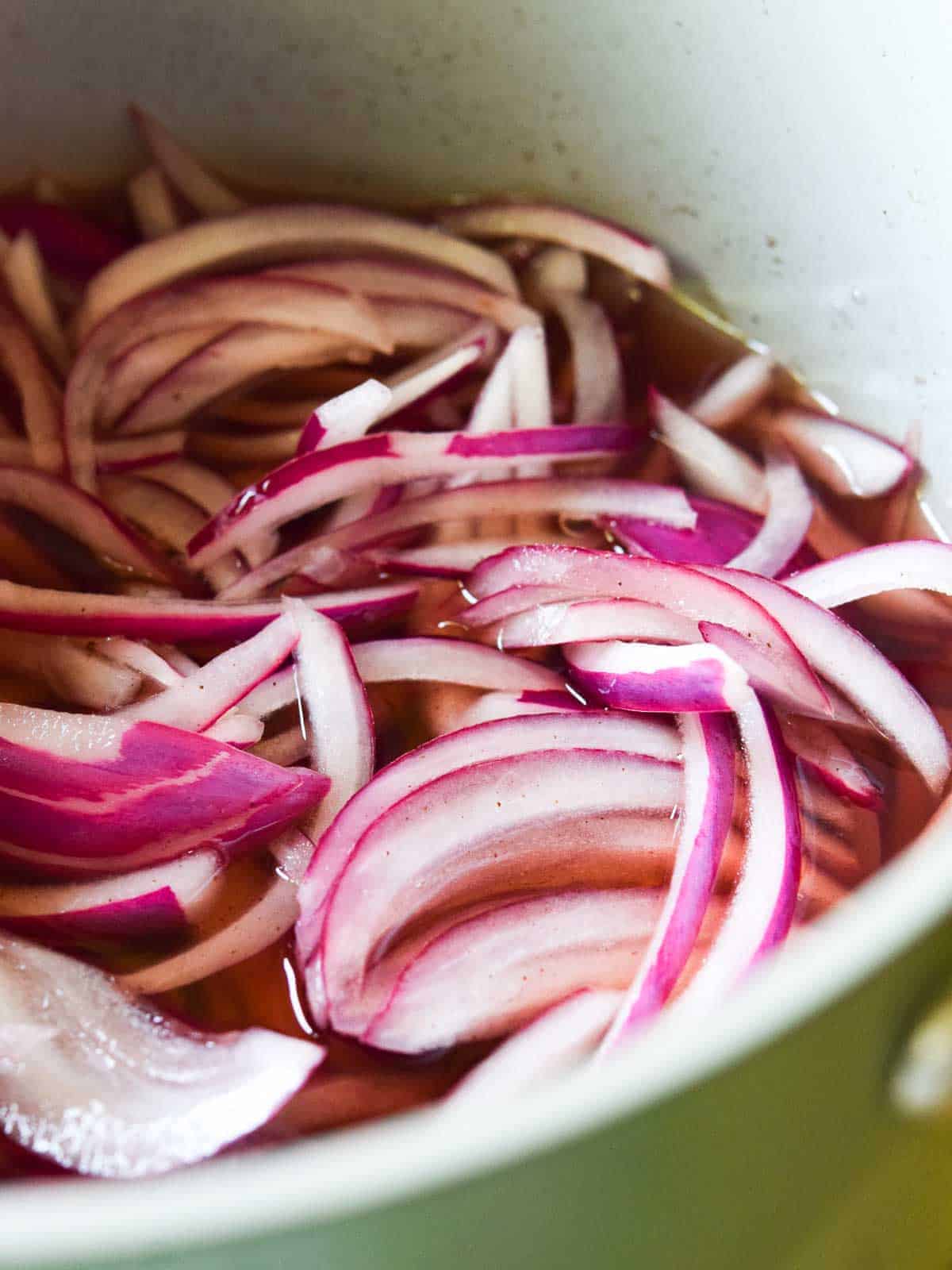 Red onions in a pot with liquid.