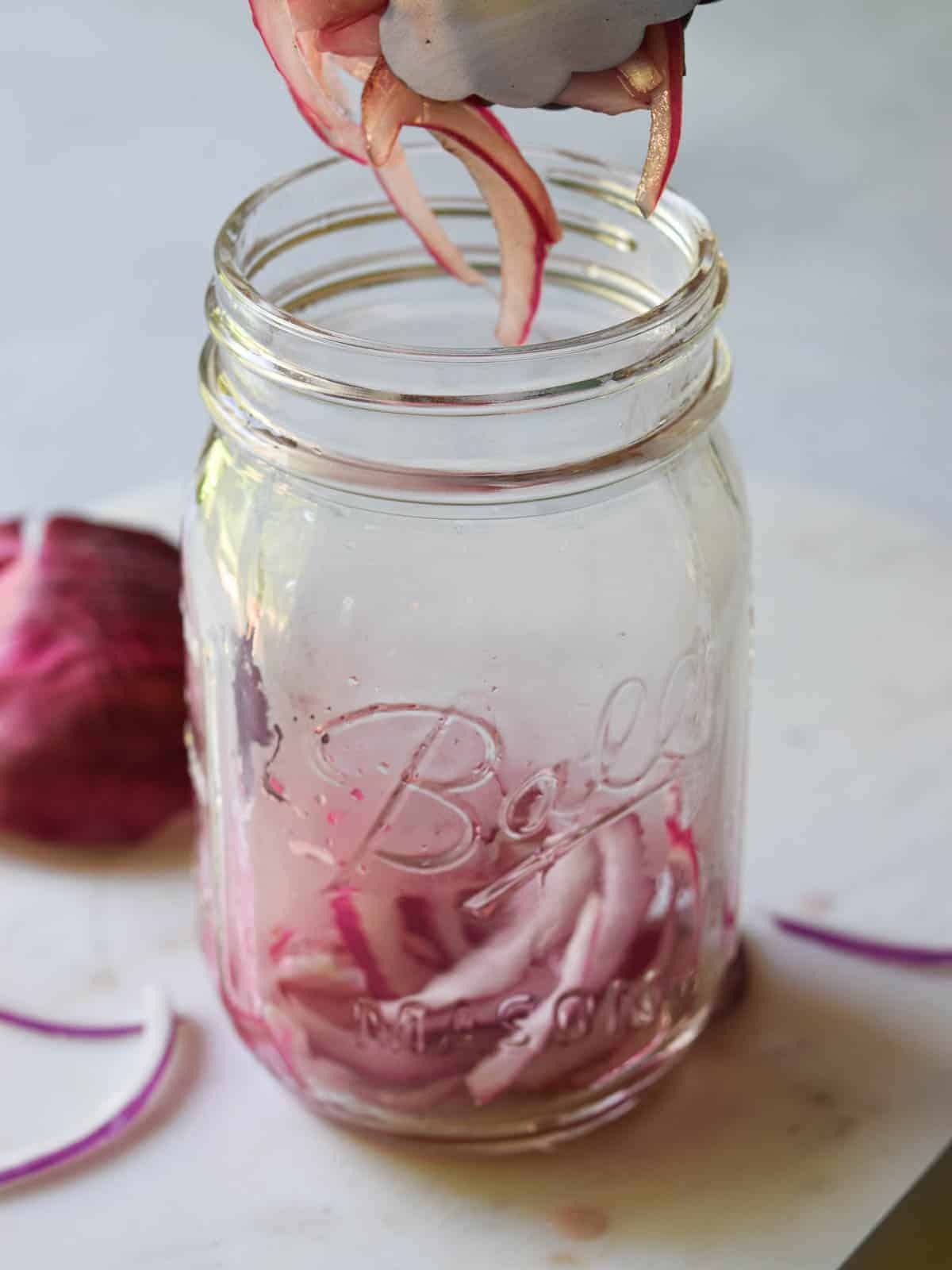 Red-onions are added to a mason jar.