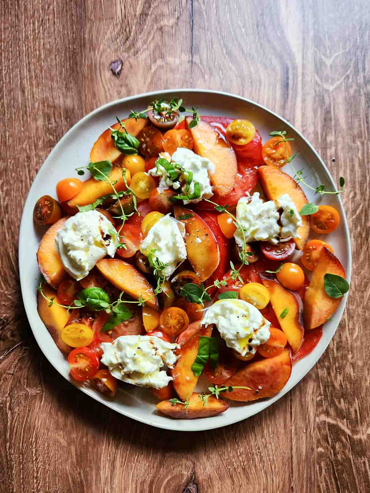 Tomatoes, peaches, and burrata on a salad plate.