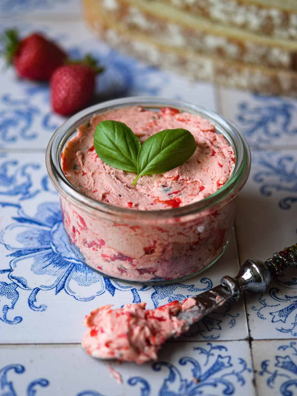 Whipped strawberry basil butter in a glass jar on a tile background.