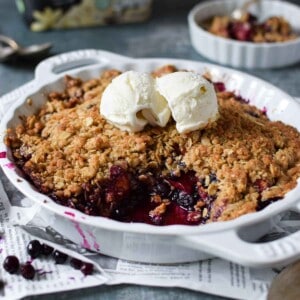 Angled view of blueberry crisp in a white plate with ice cream on top.