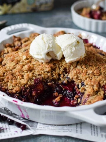 Angled view of blueberry crisp in a white plate with ice cream on top.