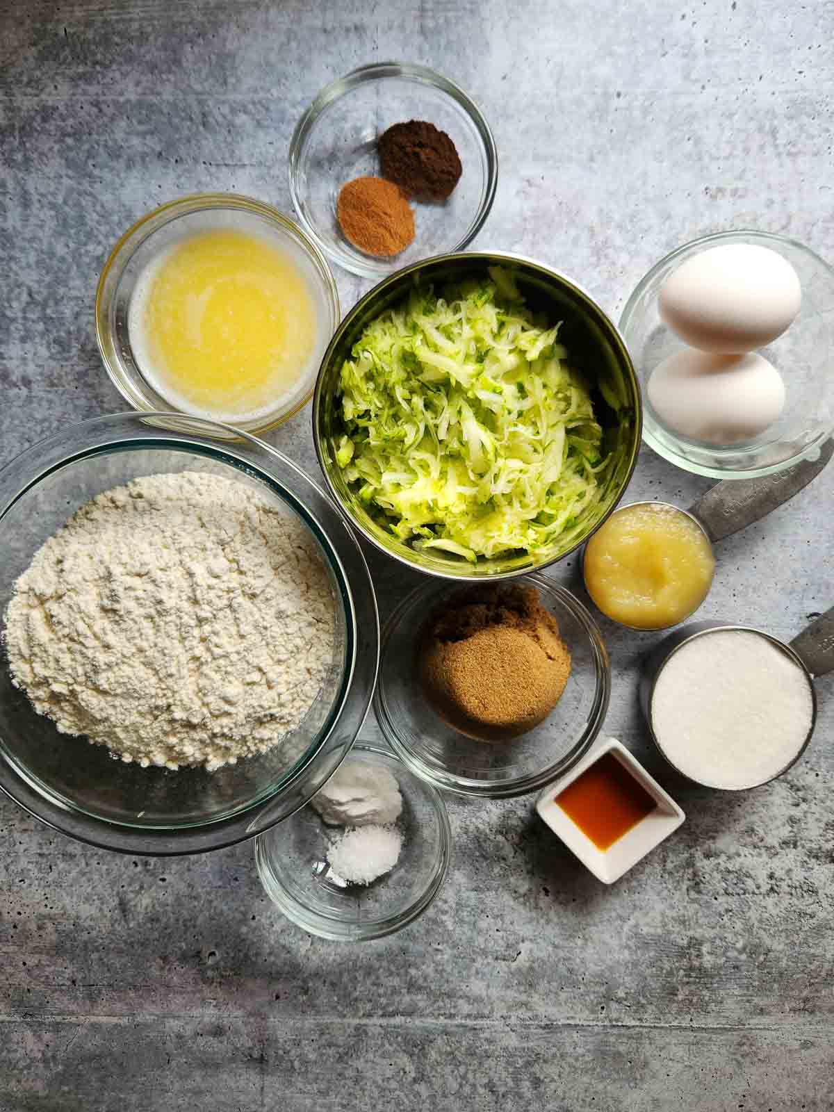 Ingredients for zucchini muffins on a concrete surface.
