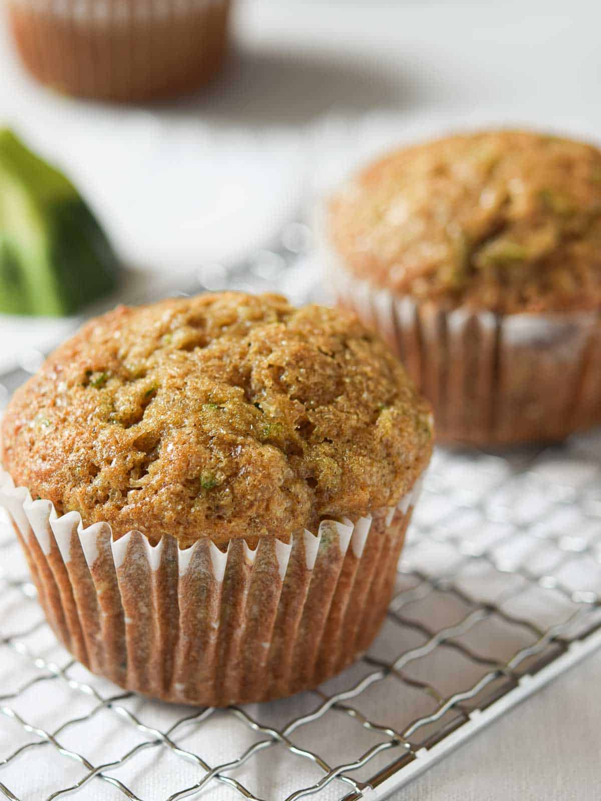 Zucchini muffins on a silver rack over a white surface.